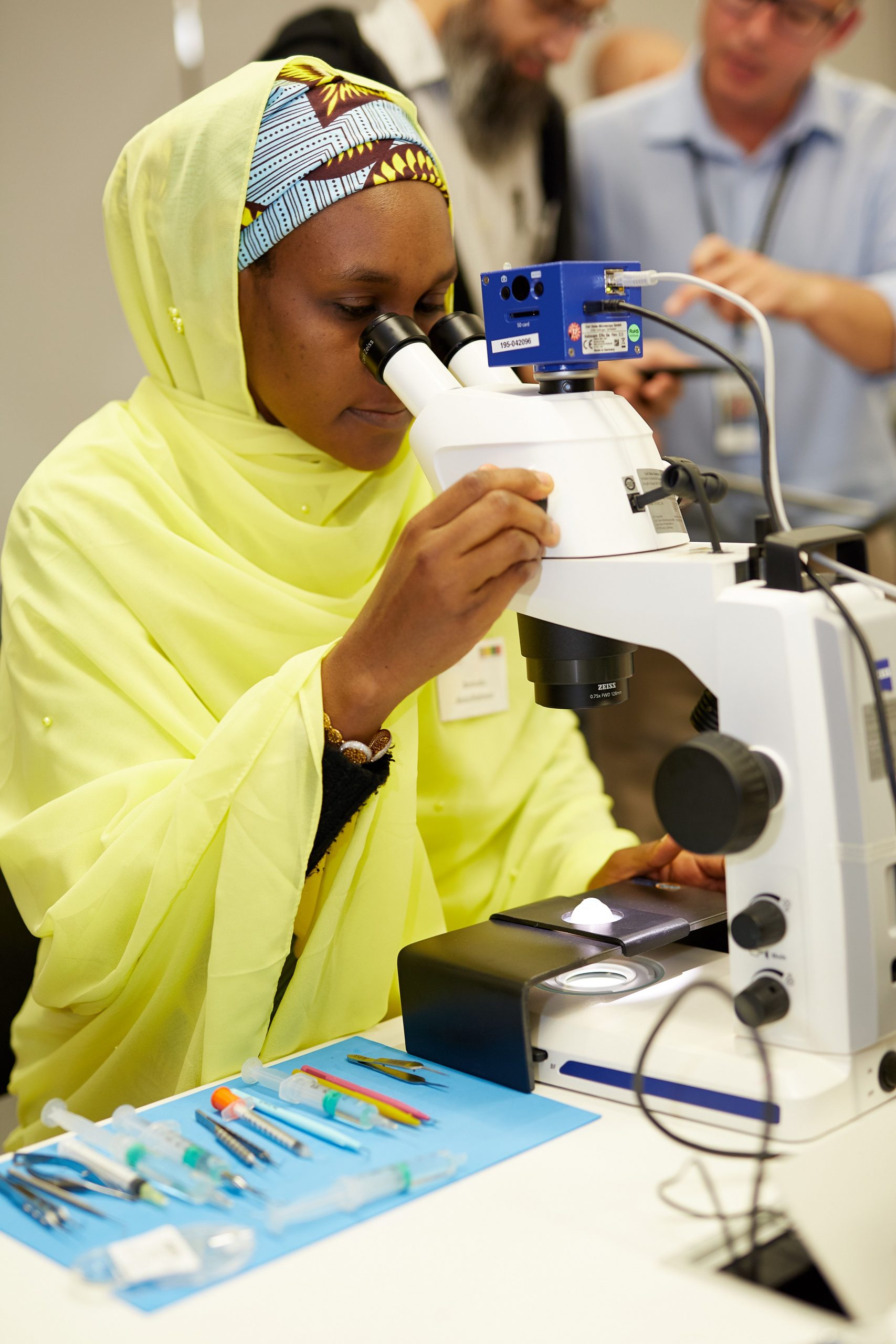 A woman in a yellow hijab uses a microscope during a surgical skills training day