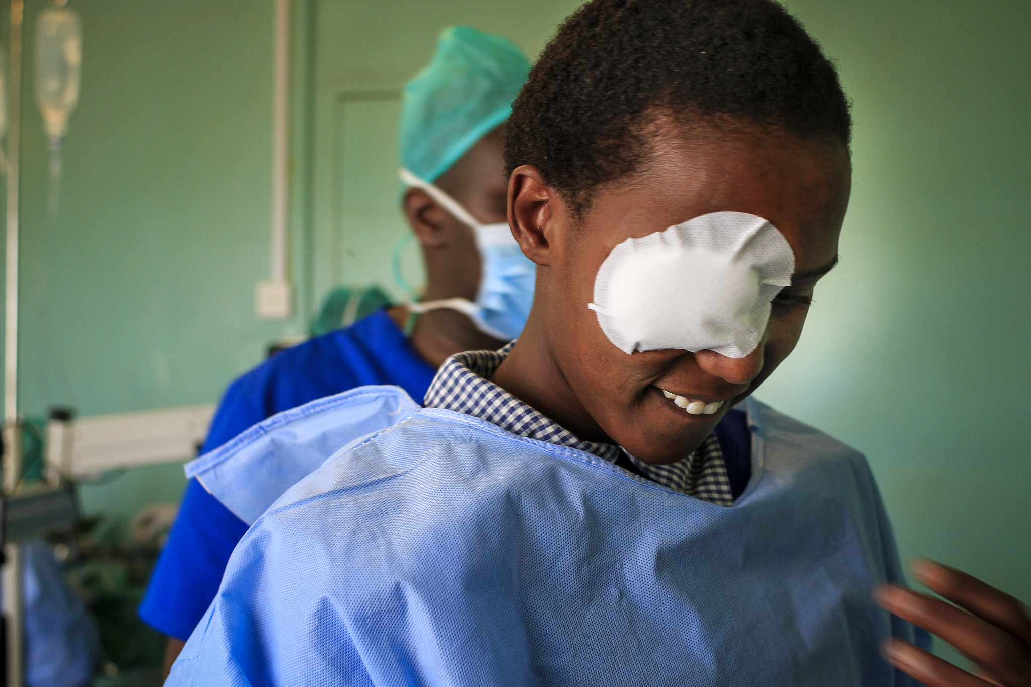 A woman in traditional robes sits on the ground following cataract surgery