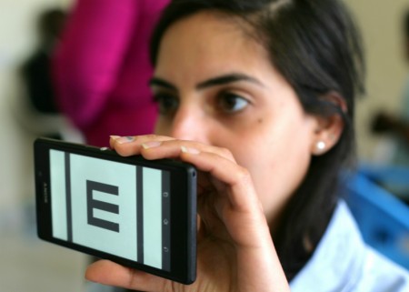 a woman holds up a smartphone with an E acuity test showing on it