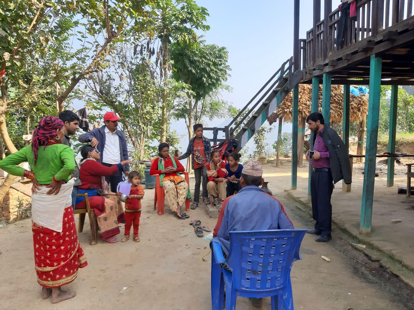 RAAB ICEH image A group of people stand outside a building. A man holds up a device for a woman in a chair whose eyes are being tested