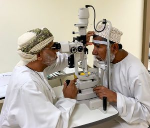 In Oman, a health worker inspects a man's eyes at a slit lamp