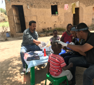 In Ethiopia, two healthcare researchers swab children's eyelids at a table outside