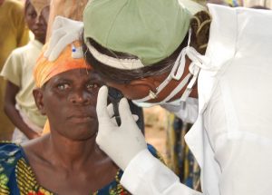 a woman with a white/blue opaque eye with a health worker inspecting the eye