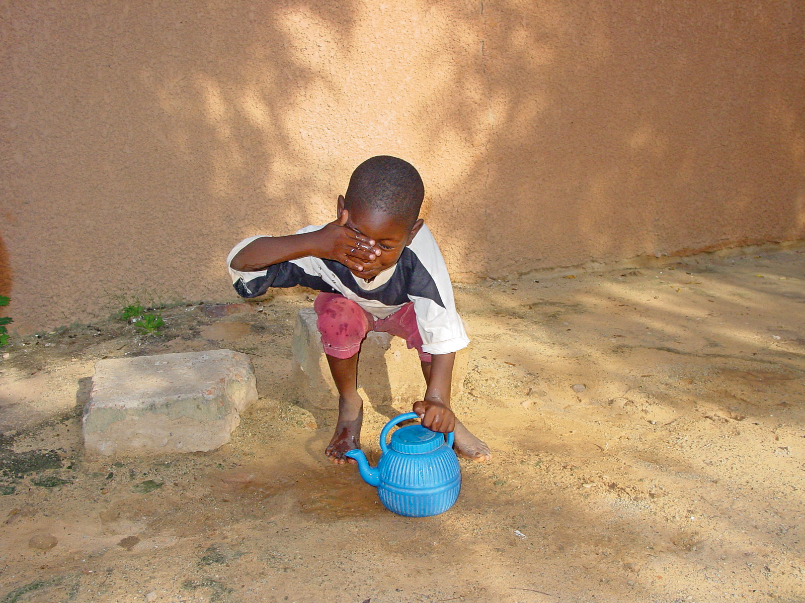 a small boy washes his face with a plastic teapot