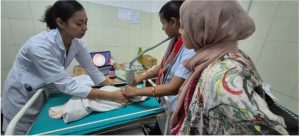 In Nepal, three health workers hold screening equipment up to a baby's eye