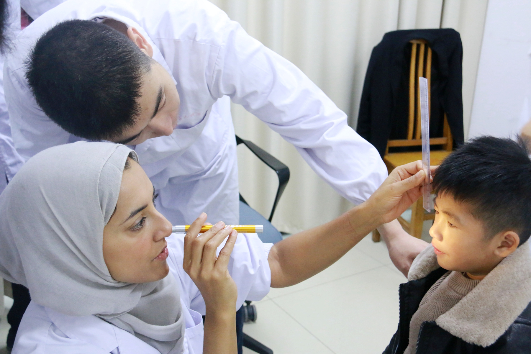 fl000014 two health workers hold a pen torch to a young boy's eye during examination