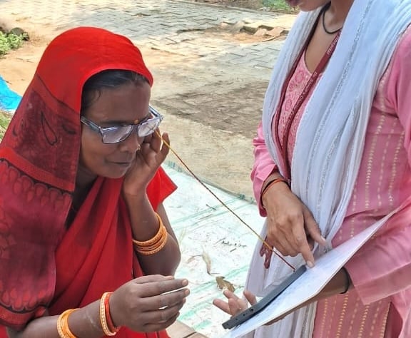 a woman in a red headdress reads with glasses as another person points to a clipboard