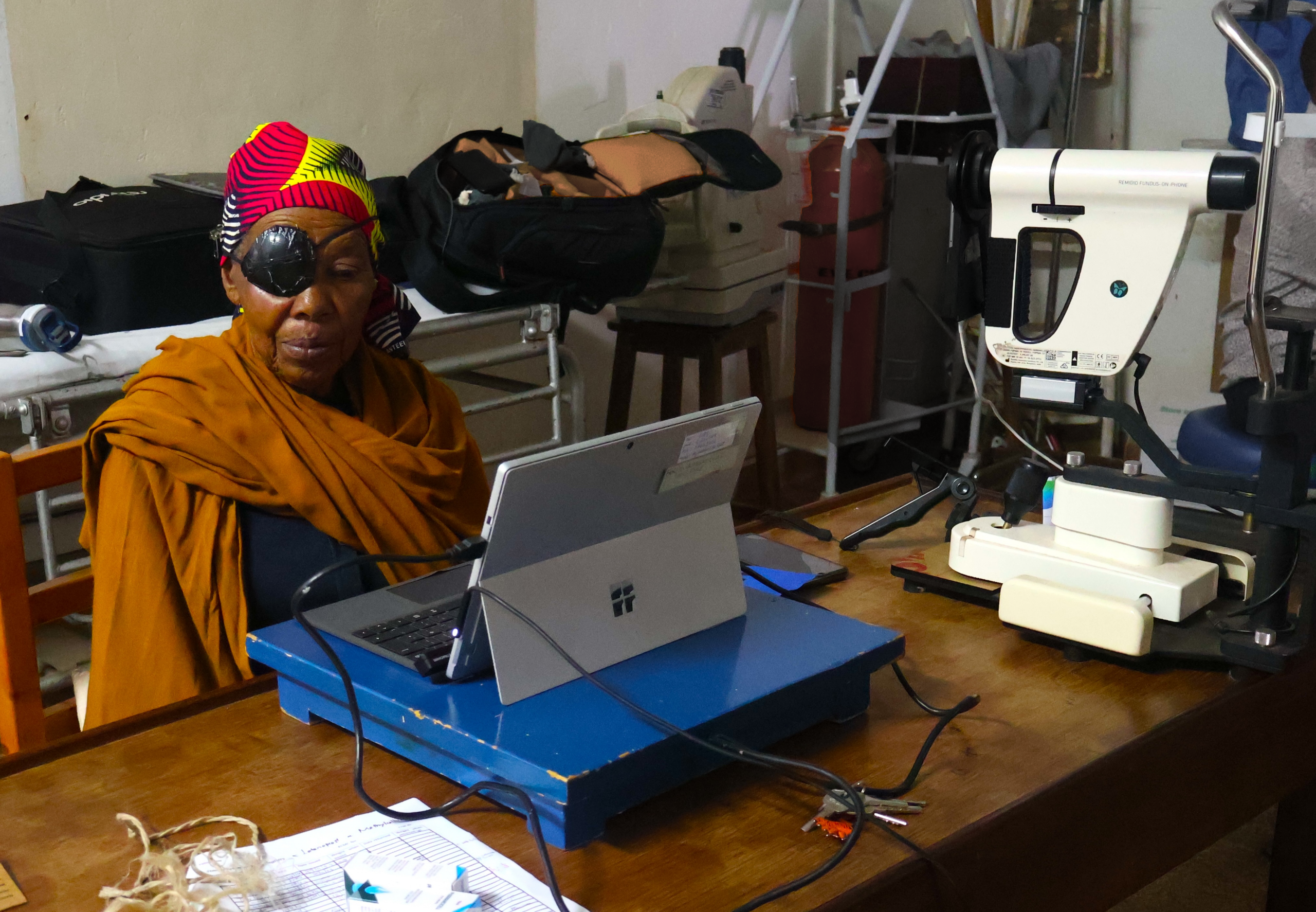 A woman in a bright headdress and an eye patch looks at a computer screen